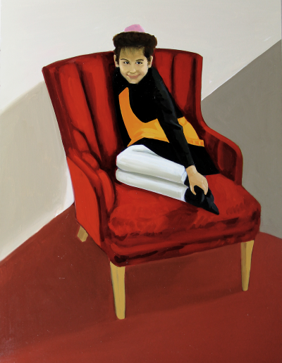 Young girl sits in a red chair with her legs curled up beneath her. She holds her right foot in her right hand. She is wearing a white pants with an orange shirt and black cardigan. Her hair is held up with a fuzzy pink ball.